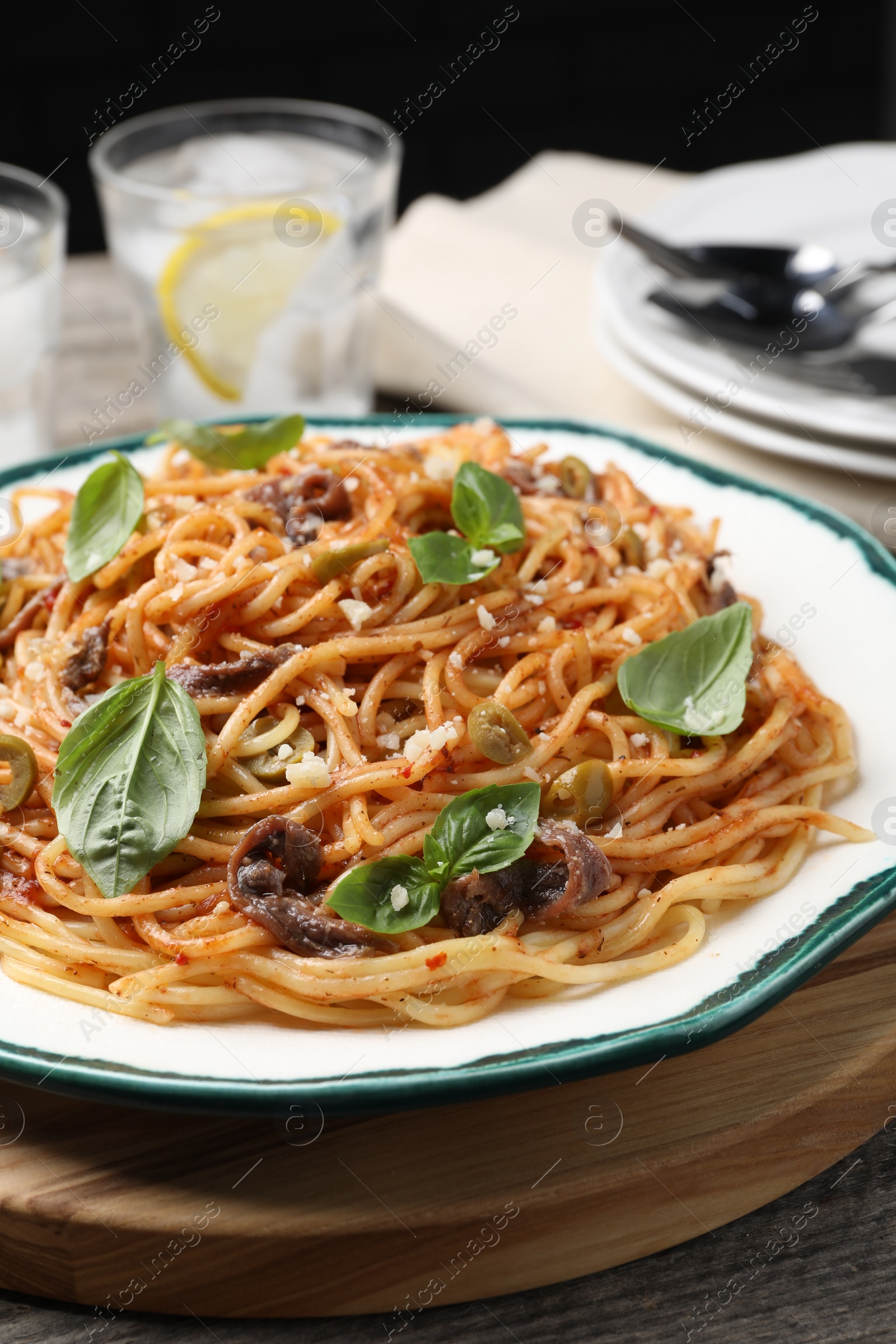 Photo of Delicious pasta with anchovies, tomato sauce and basil on wooden table