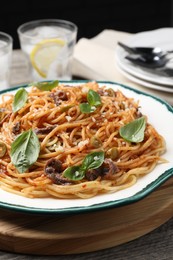 Photo of Delicious pasta with anchovies, tomato sauce and basil on wooden table