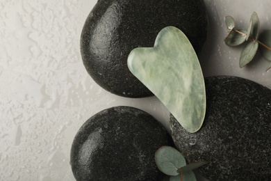 Jade gua sha tool, spa stones and eucalyptus branches on grey table, flat lay