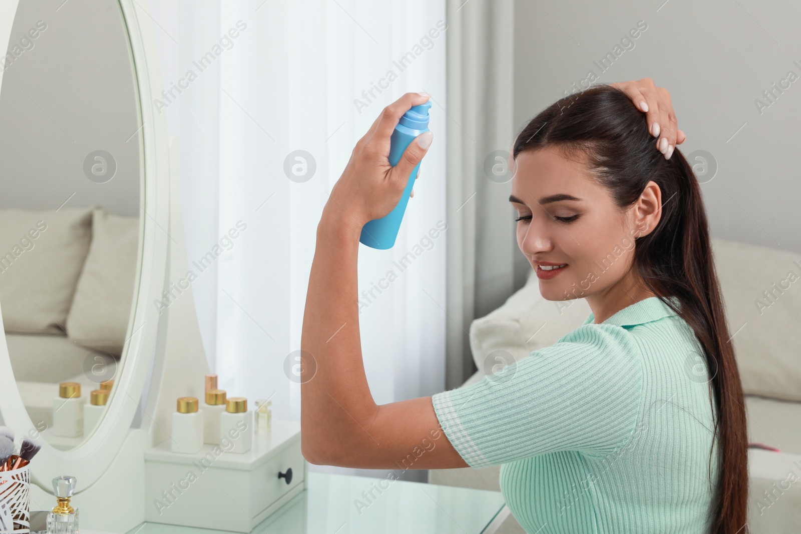 Photo of Woman applying dry shampoo onto her hair near mirror at home