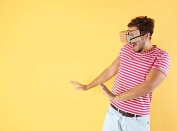 Photo of Young man using cardboard virtual reality headset on color background. Space for text