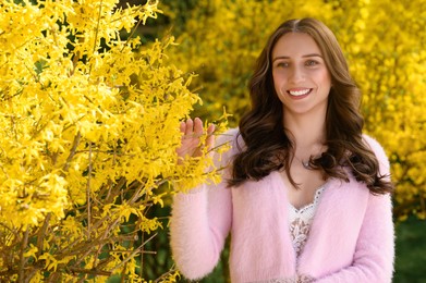 Beautiful young woman near blossoming shrub on spring day