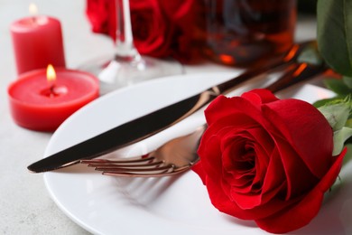 Photo of Beautiful place setting with dishware, candles and rose for romantic dinner on light table, closeup