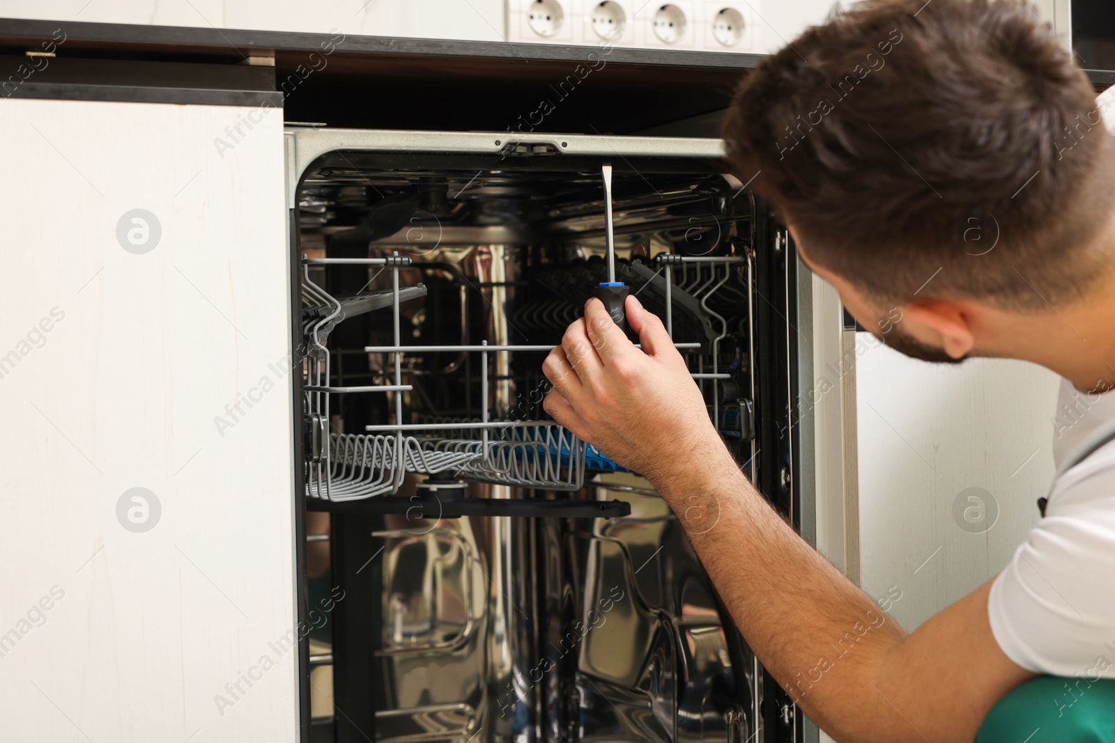 Photo of Serviceman repairing dishwasher with screwdriver, closeup view