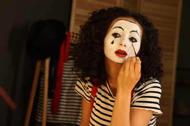 Photo of Young woman applying mime makeup near mirror indoors