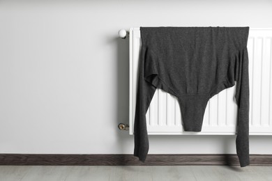 Grey turtleneck sweater hanging on white radiator in room. Space for text
