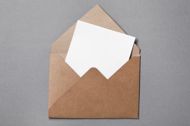 Blank sheet of paper in open letter envelope on grey background, top view