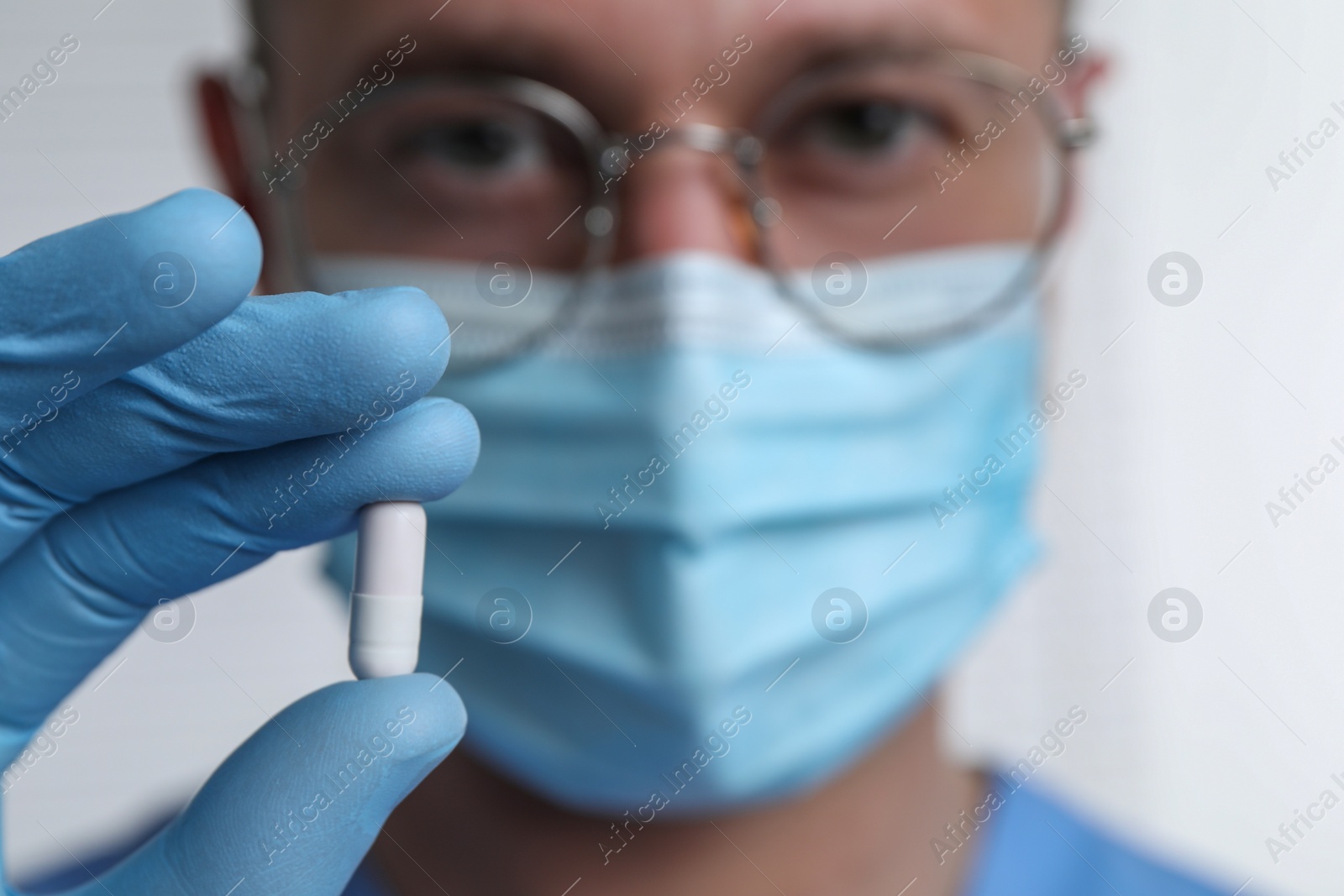 Photo of Doctor holding pill on light background, selective focus. Space for text