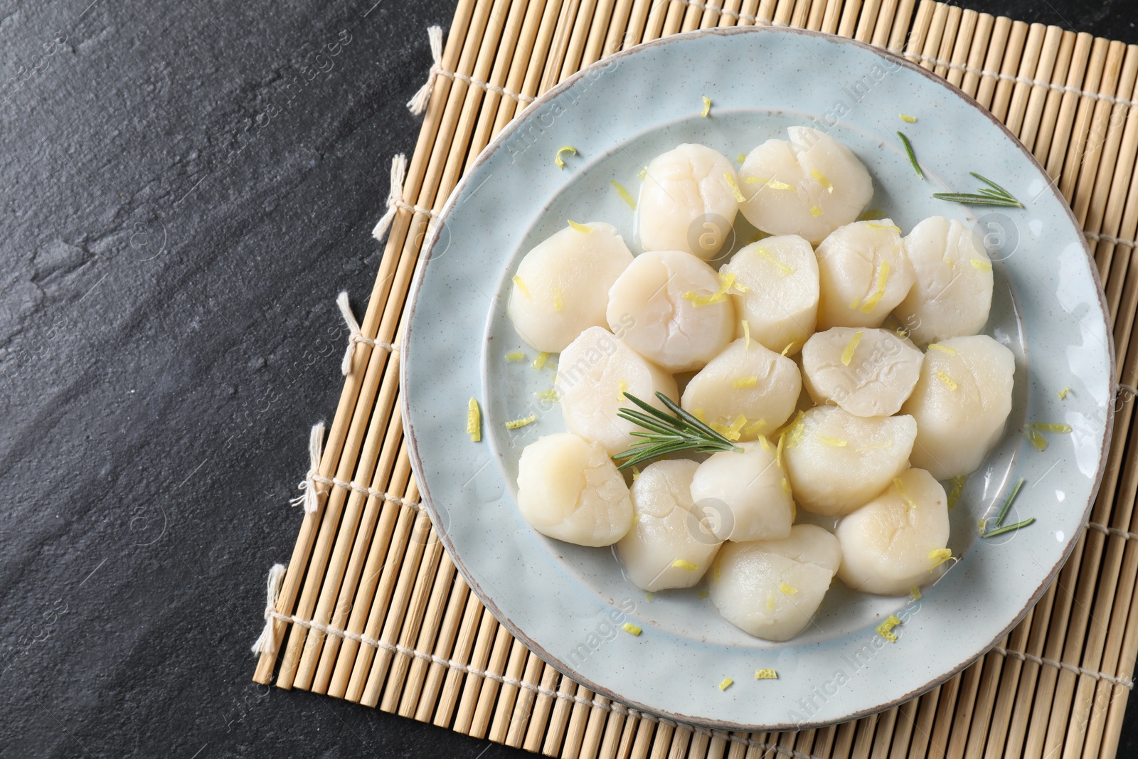 Photo of Raw scallops with lemon and rosemary on dark textured table, top view