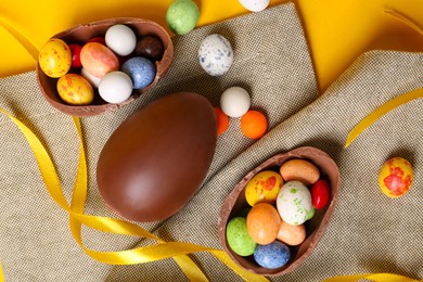 Tasty chocolate eggs with candies and ribbon on cloth, flat lay