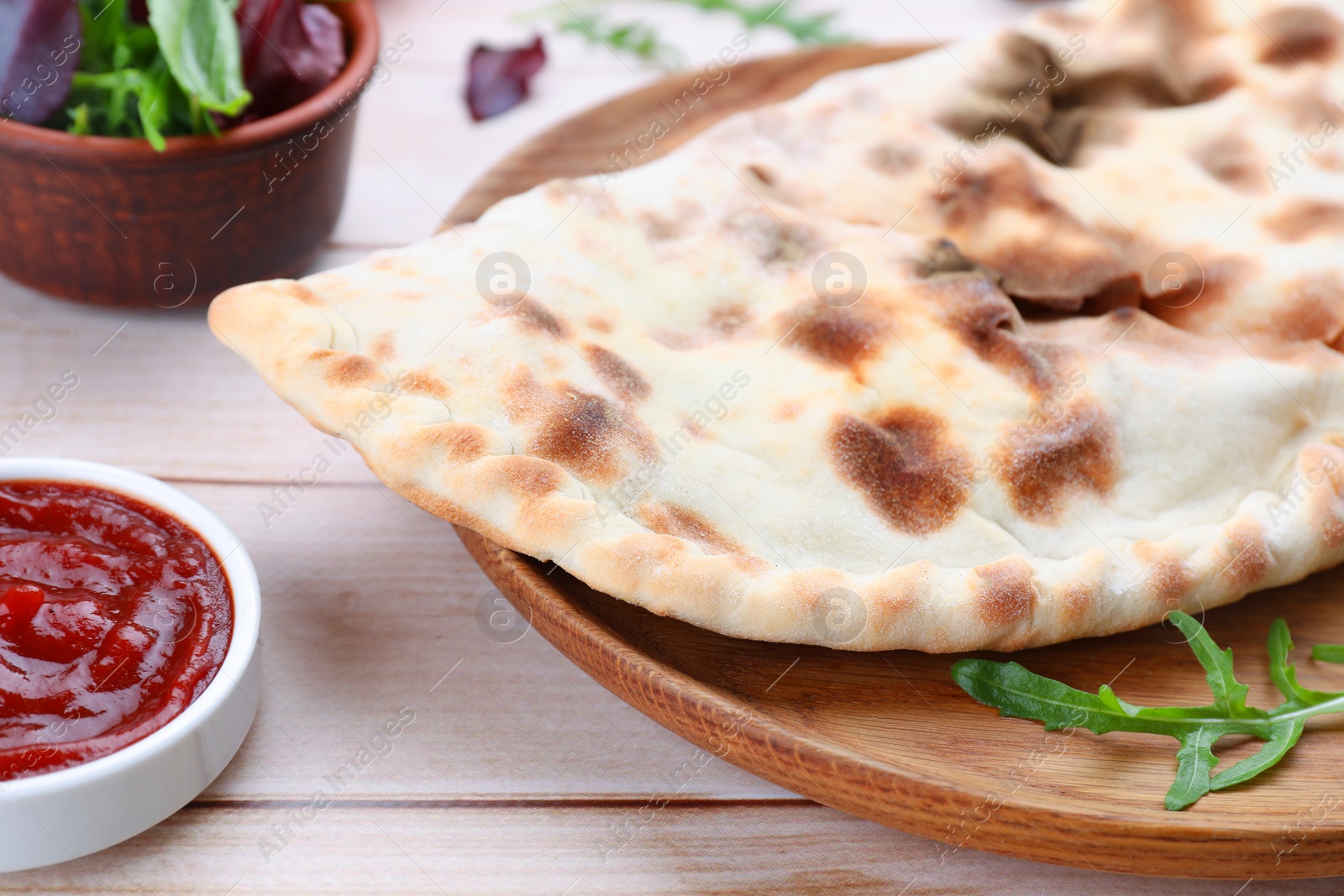 Photo of Delicious calzone on light wooden table, closeup