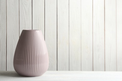 Photo of Stylish pink ceramic vase on white wooden table. Space for text