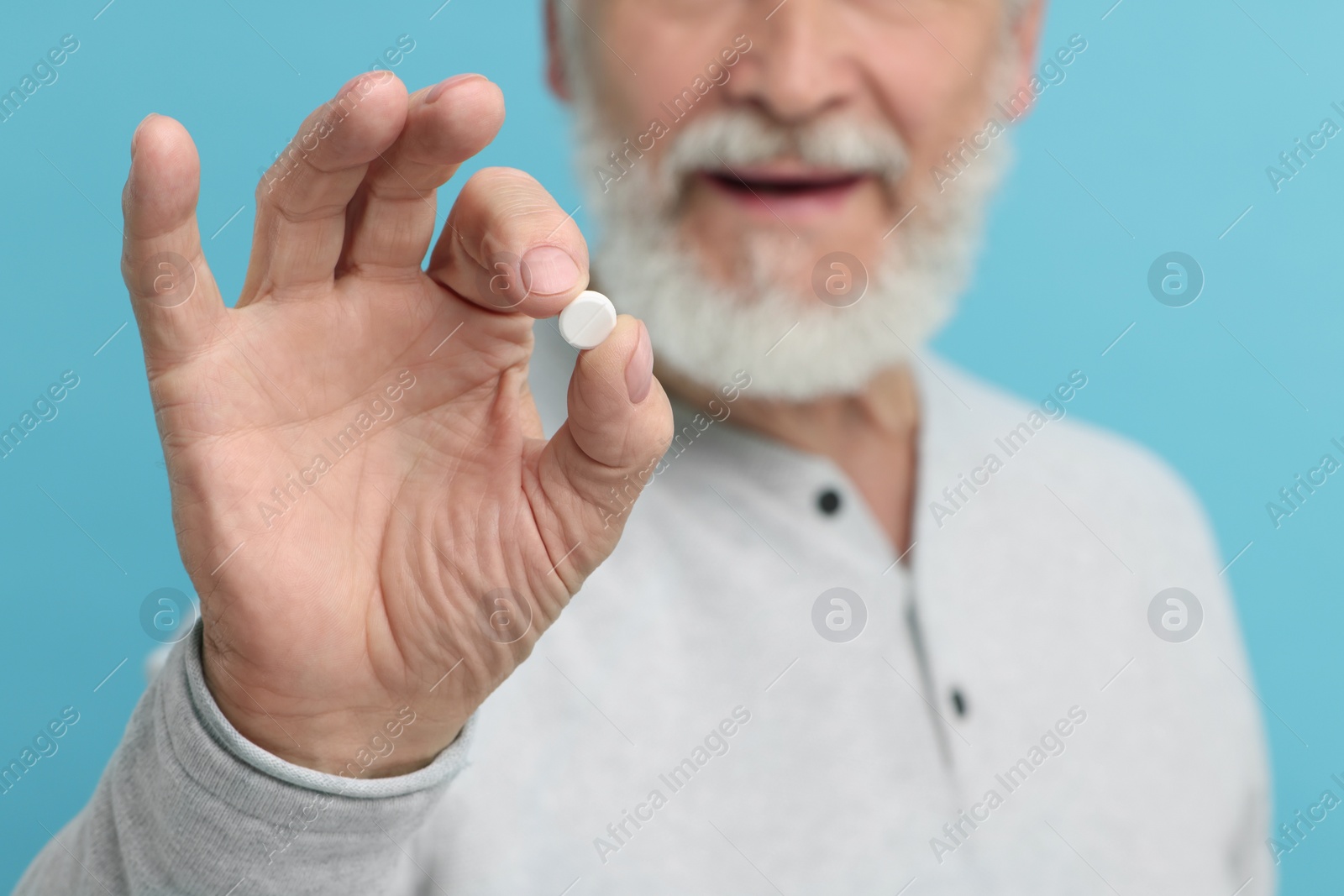 Photo of Senior man with pill on light blue background, closeup