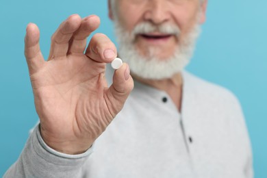 Senior man with pill on light blue background, closeup