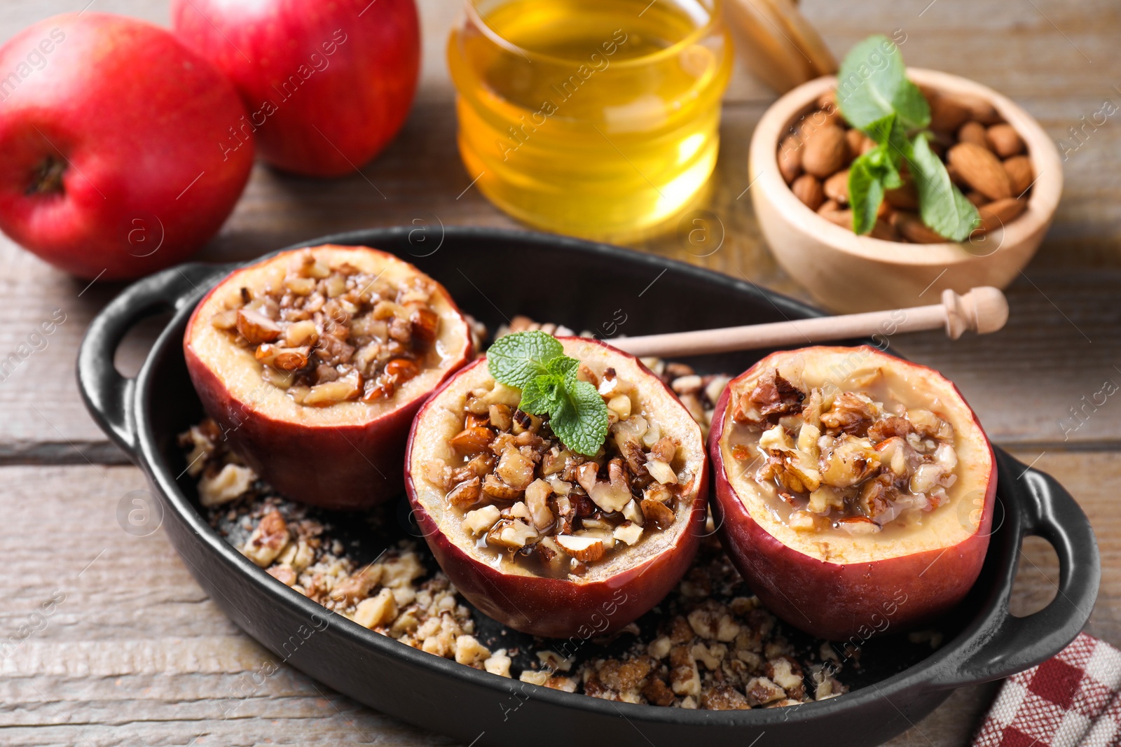 Photo of Tasty baked apples with nuts, honey and mint in baking dish on wooden table, closeup