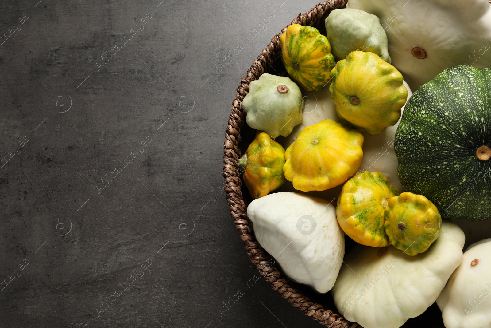 Photo of Fresh ripe pattypan squashes in wicker bowl on grey table, top view. Space for text