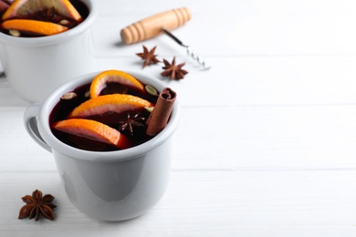 Photo of Aromatic mulled wine on white wooden table. Space for text