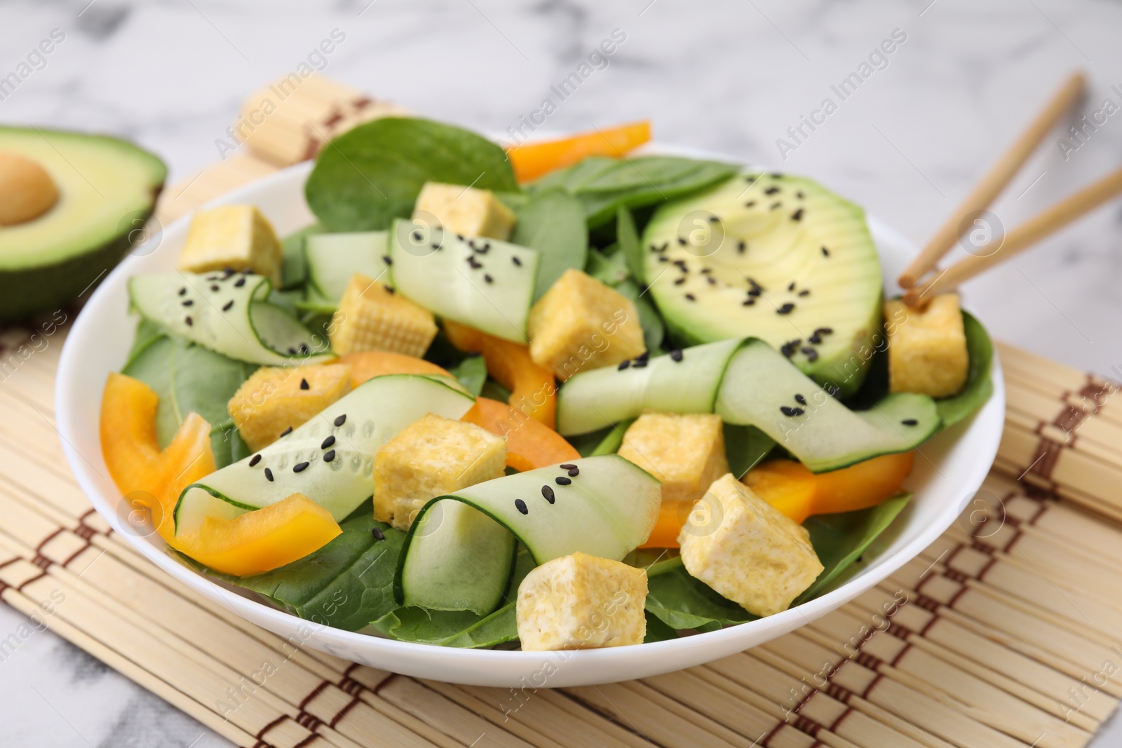 Photo of Bowl of tasty salad with tofu and vegetables on white marble table, closeup