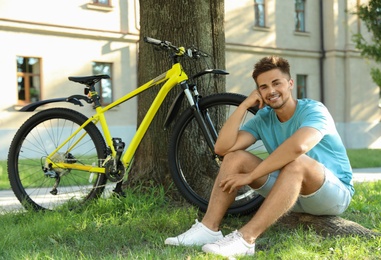 Handsome young man sitting near bicycle on green grass