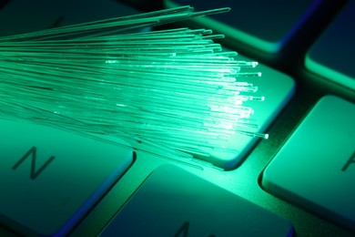 Optical fiber strands transmitting green light on computer keyboard, macro view
