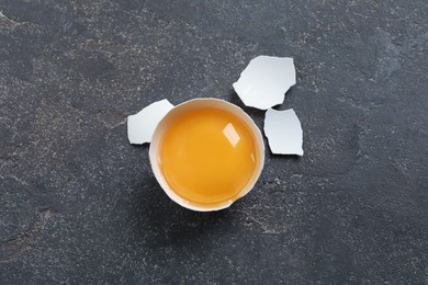 Cracked eggshell with raw yolk on grey table, top view