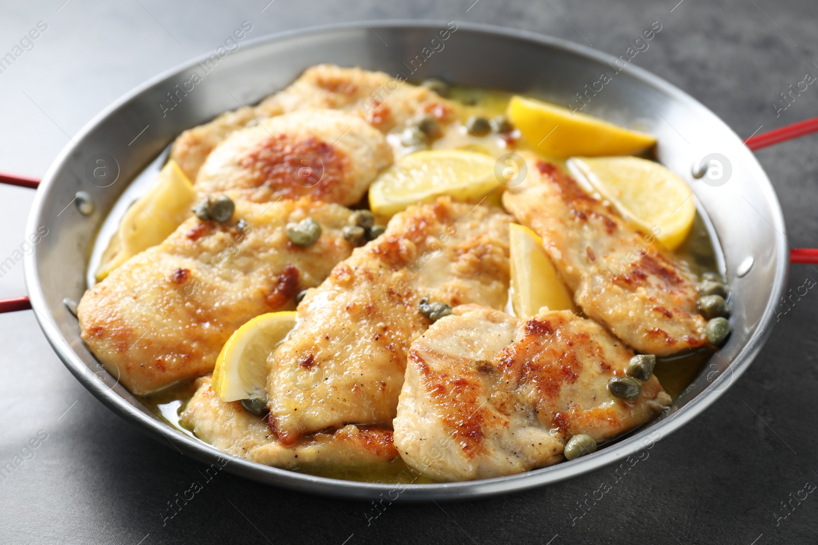 Photo of Delicious chicken piccata with lemons on grey table, closeup