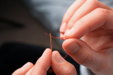 Photo of Woman threading sewing needle on blurred background, closeup