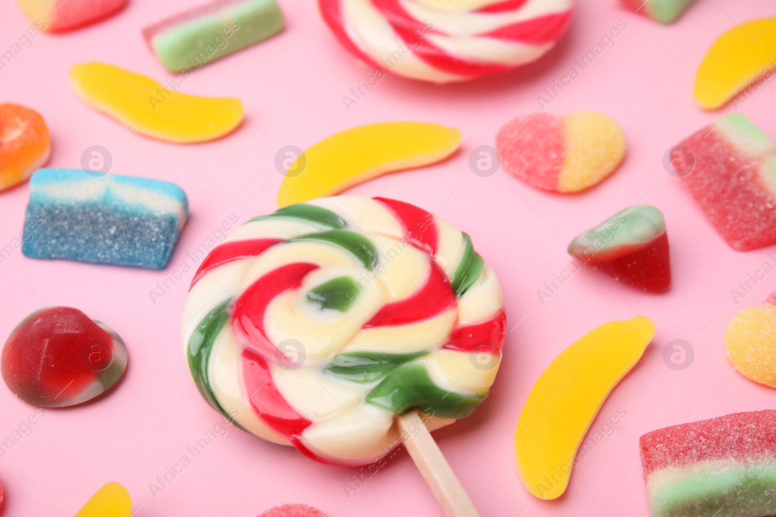 Photo of Many different jelly candies and lollipop on pink background, closeup