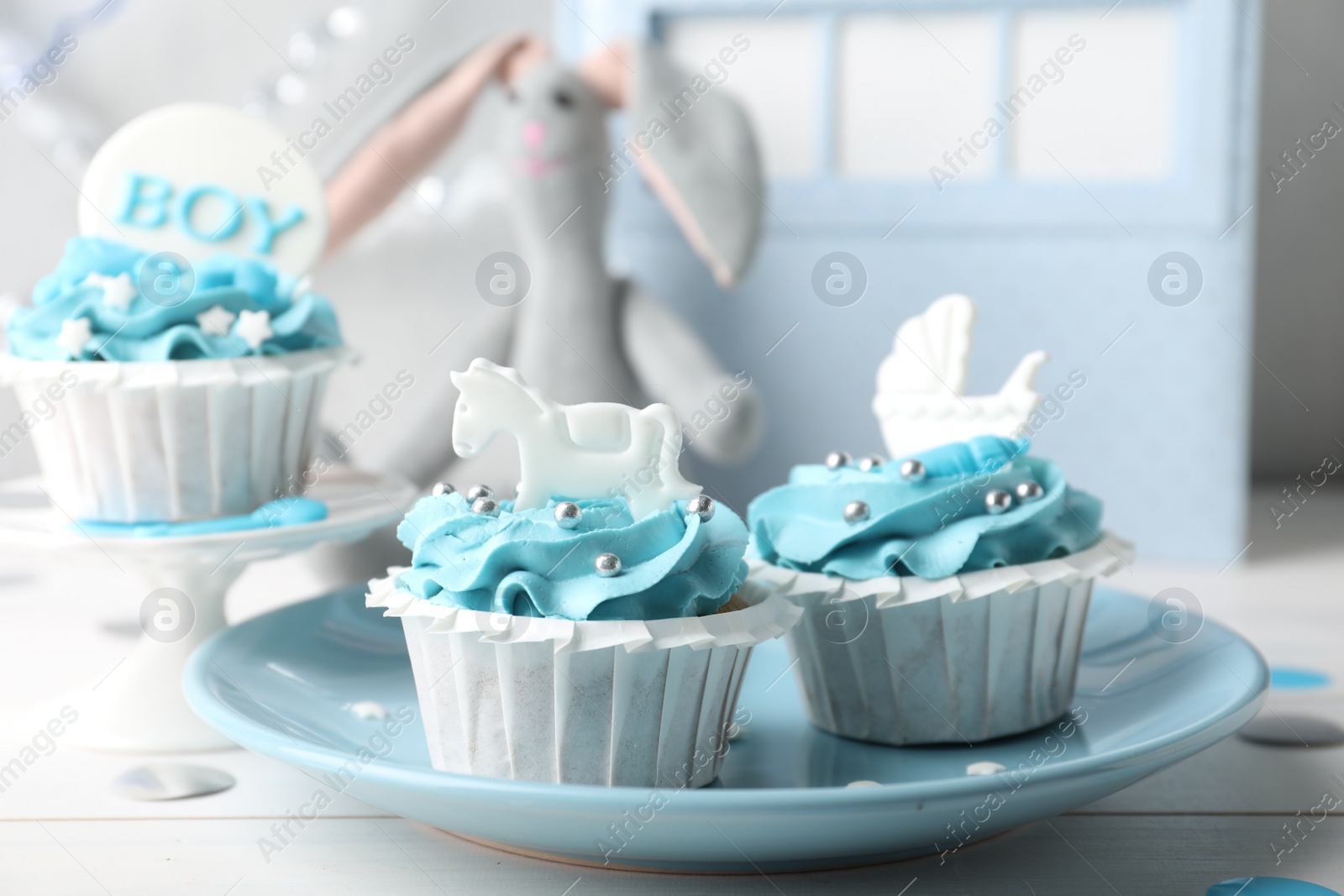 Photo of Delicious cupcakes with light blue cream and toppers for baby shower on white wooden table