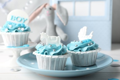 Delicious cupcakes with light blue cream and toppers for baby shower on white wooden table