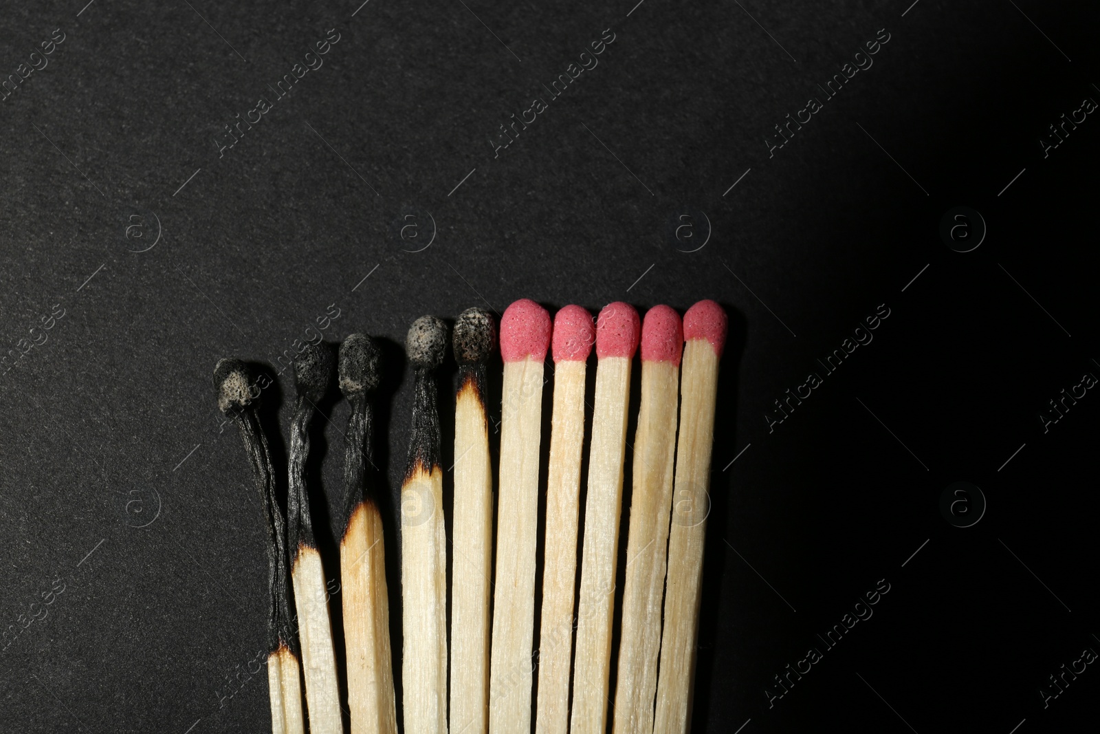Photo of Burnt and whole matches on black background, flat lay. Stop destruction concept