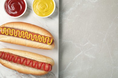 Photo of Fresh delicious hot dogs with sauces on light grey marble table, top view. Space for text