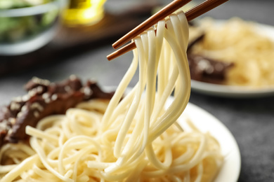 Chopsticks with tasty cooked rice noodles over plate, closeup