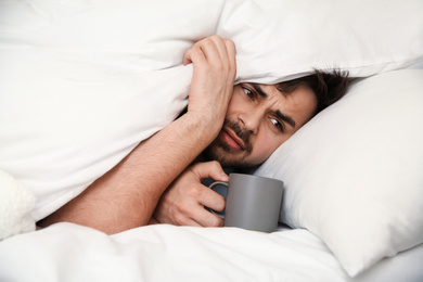 Photo of Sick young man with cup of hot drink in bed at home. Influenza virus