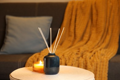 Aromatic reed air freshener and scented candle on wooden table indoors