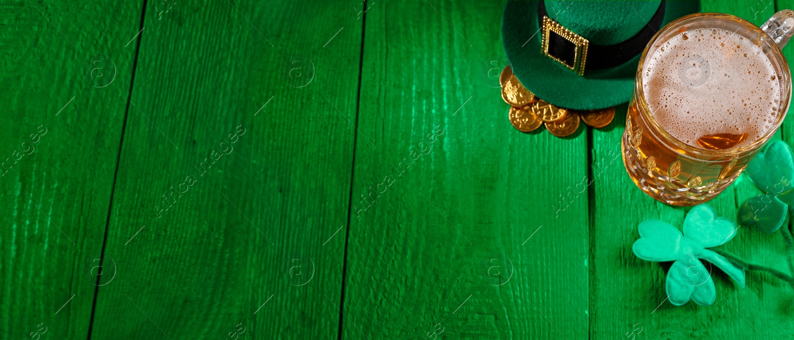 Image of St. Patrick's day. Beer, leprechaun hat, gold and decorative clover leaves on green wooden table. Banner design with space for text