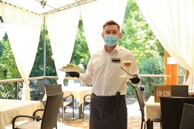 Photo of Waiter serving salad and coffee in restaurant. Catering during coronavirus quarantine