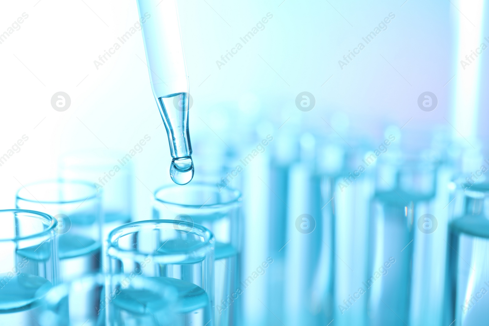 Photo of Dripping liquid from pipette into test tube on light blue background, closeup