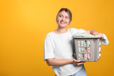 Photo of Happy woman with basket full of laundry on orange background. Space for text