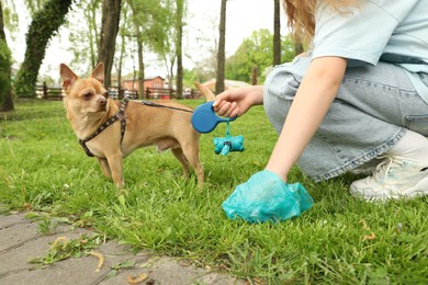 Woman picking up her dog's poop from green grass in park, closeup