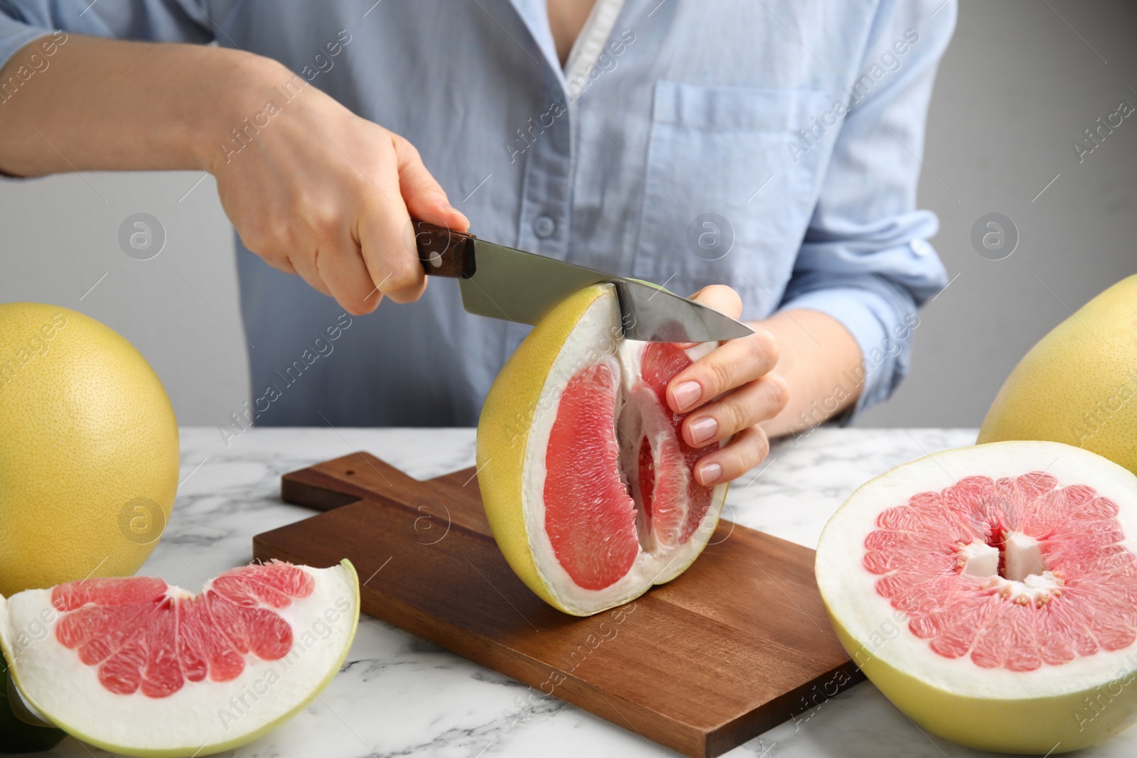 Photo of Woman cutting tasty red pomelo at white marble table, closeup