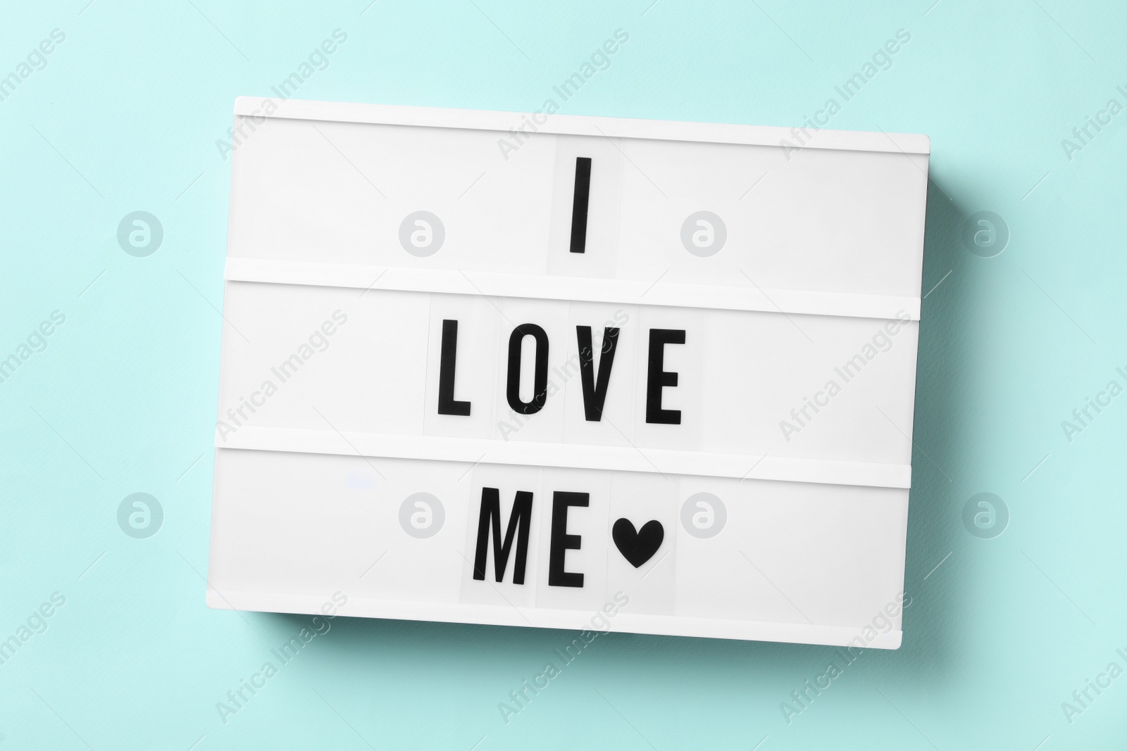 Photo of Light box with phrase I Love Me on blue background, top view