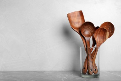 Photo of Set of wooden kitchen utensils in glass holder on light grey marble table. Space for text