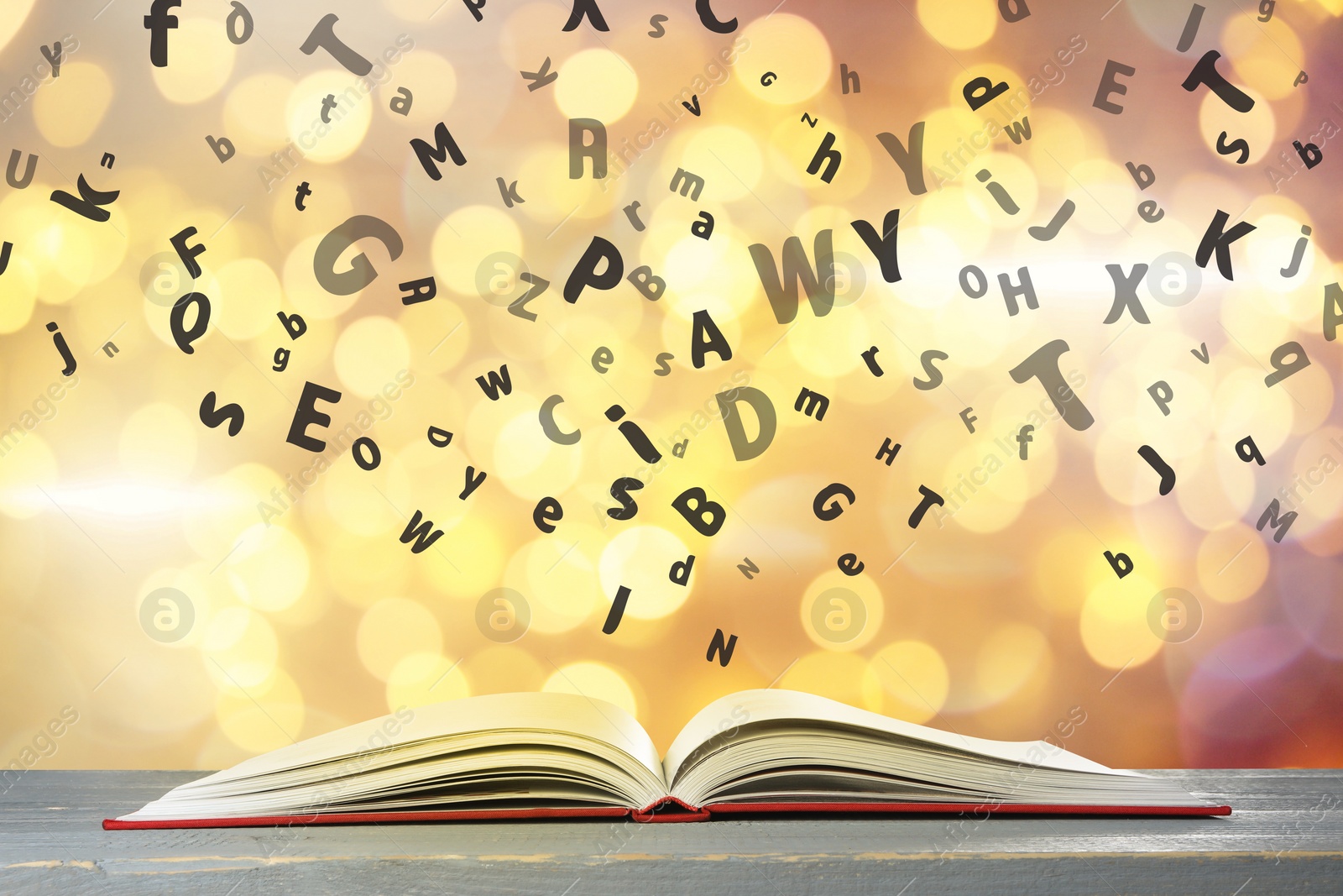 Image of Letters flying out from open book on wooden table, bokeh effect