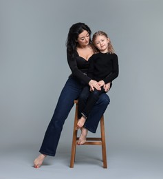 Beautiful mother with little daughter on stool against grey background