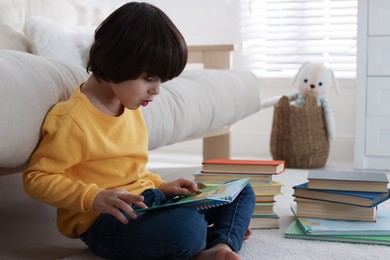 Photo of Cute little boy reading book on floor at home