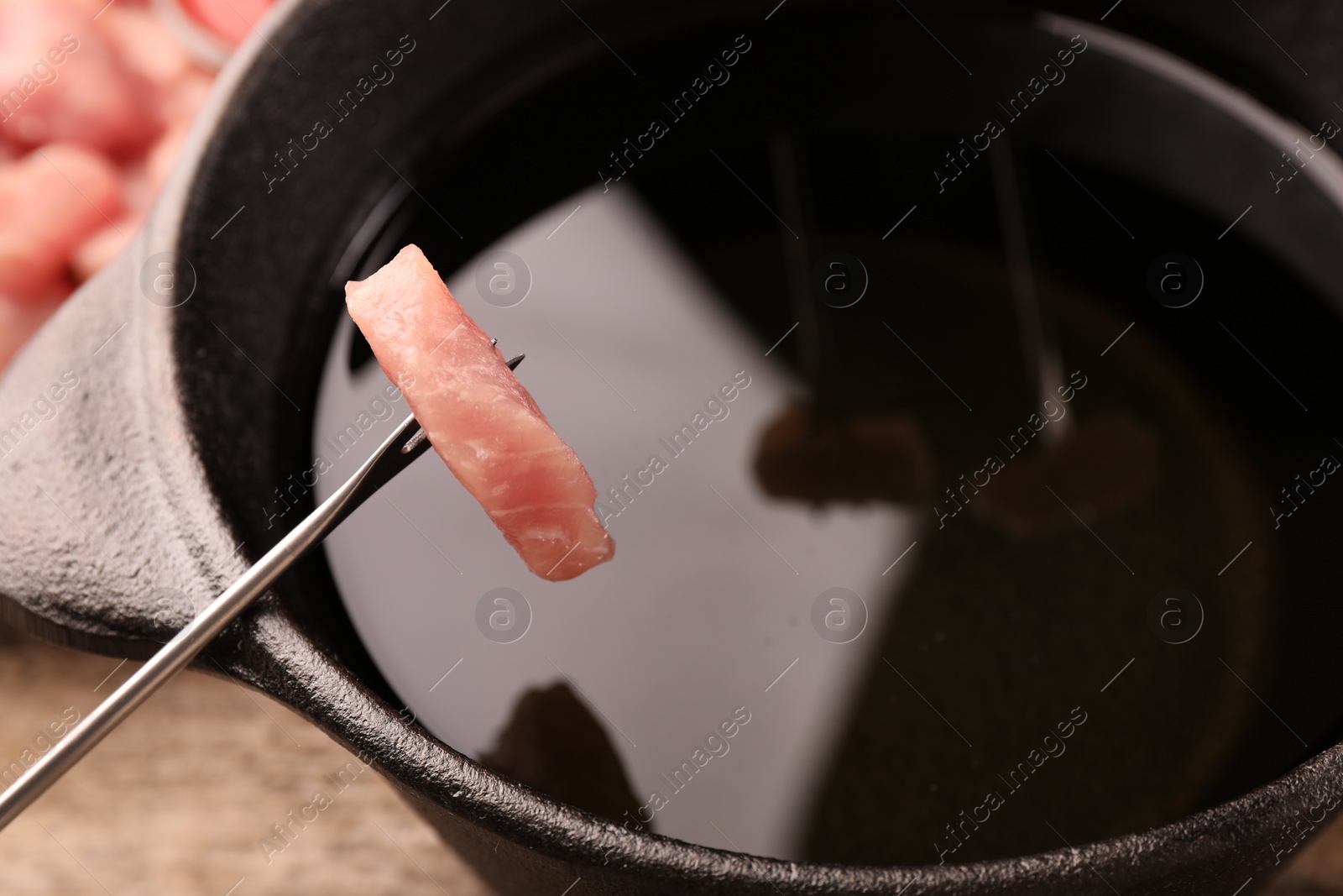 Photo of Fondue pot and fork with piece of raw meat on wooden table, closeup