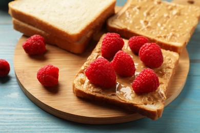 Photo of Delicious toasts with peanut butter and raspberries on light blue wooden table, closeup