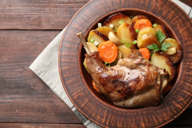 Photo of Tasty cooked rabbit meat with vegetables on wooden table, top view. Space for text