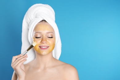 Photo of Beautiful woman applying natural mask on her face against color background. Space for text